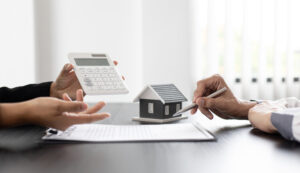Real estate agent and client signing papers with a calculator, and a house model.